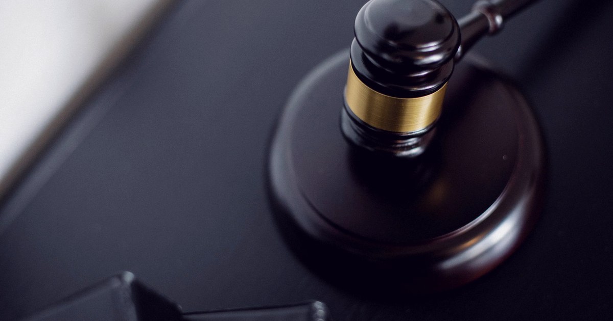 A wooden judge's gavel resting on its round sound block on a dark desk