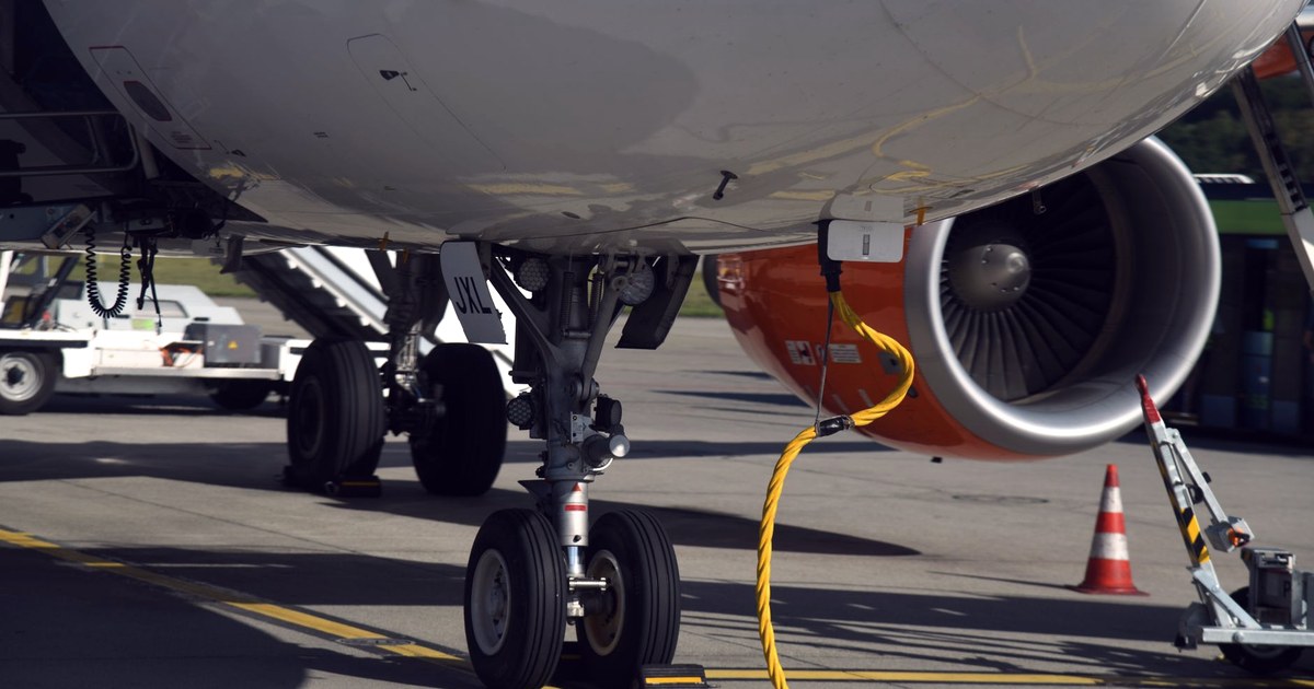 Close-up of a jet's landing gear and engine on an airport tarmac, with a safety cone beside the wheels