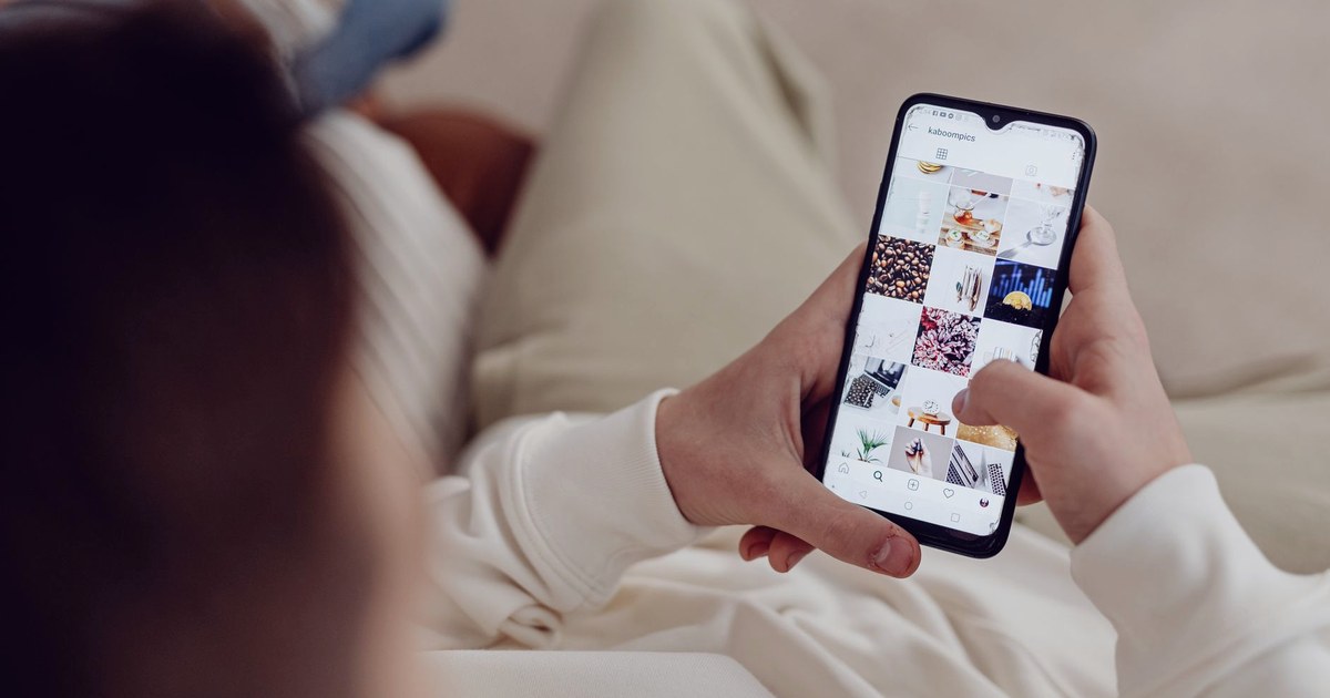 A person scrolling a grid of photos in a social media app on a smartphone, held in both hands