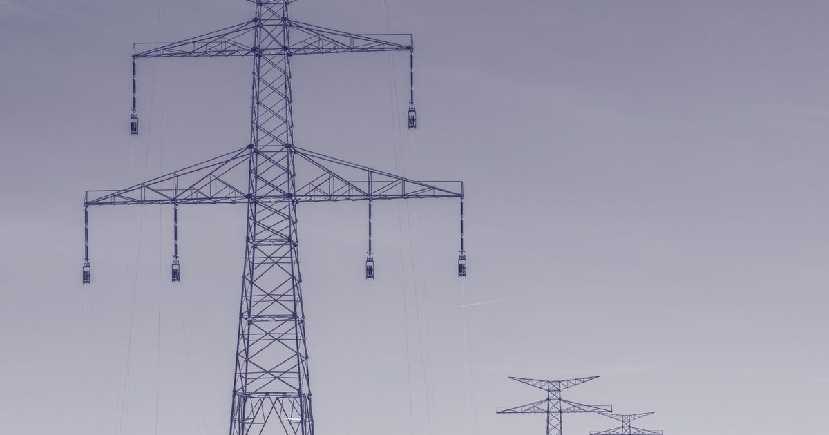 Electricity transmission towers of two different scales against a clear blue sky, evoking a cross-border power grid
