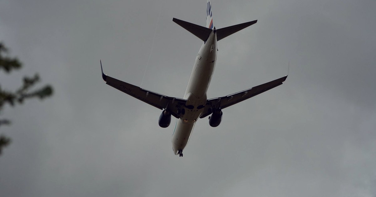 A commercial jet aircraft seen from below with landing gear extended, approaching under a heavy cloudy sky