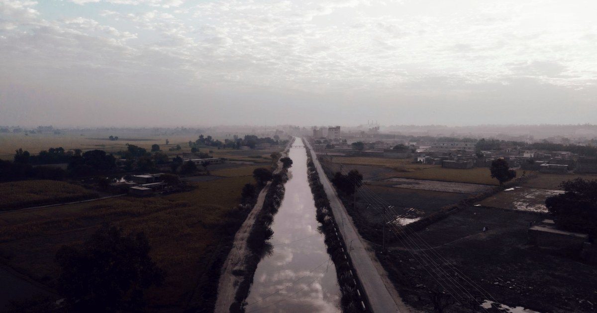 Aerial view of an irrigation canal running through farmland on a hazy morning near Gujranwala, Punjab, Pakistan
