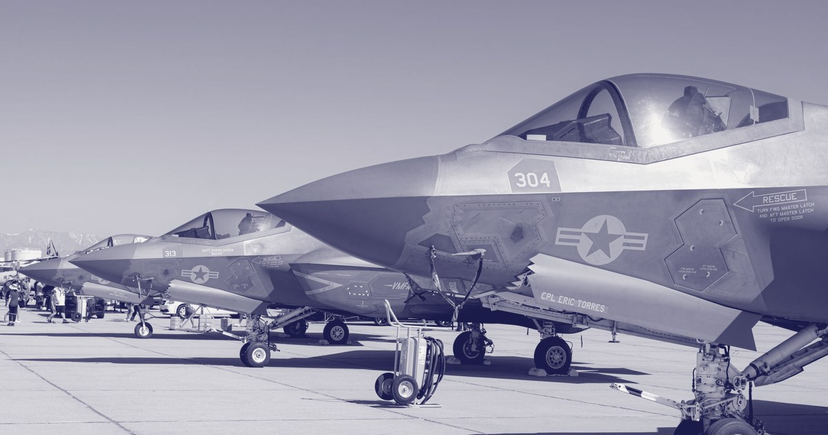 A row of F-35 fighter jets parked on the tarmac, their canopies open, at a US air base
