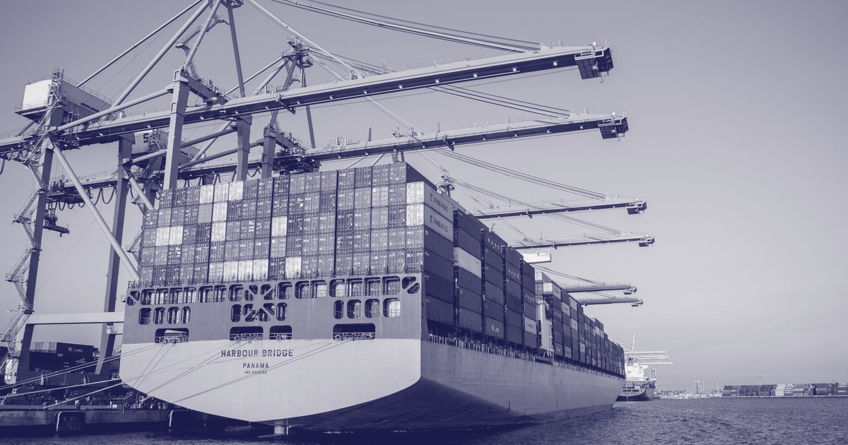 A container port at sunset, cranes loading stacked cargo containers beside a quiet harbor