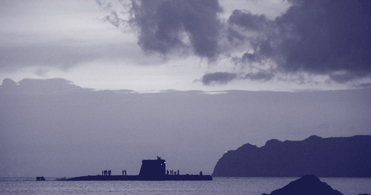 A submarine surfaced near a coastline at dusk, silhouetted against a cloudy sky