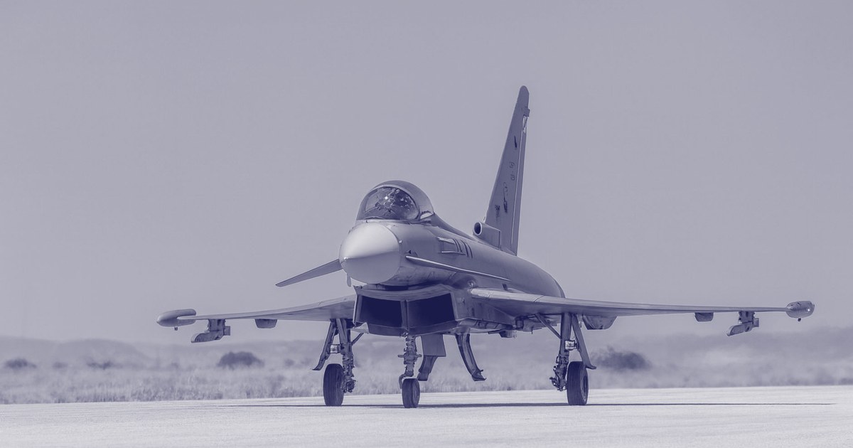 A fighter jet on an airbase runway under a clear blue sky
