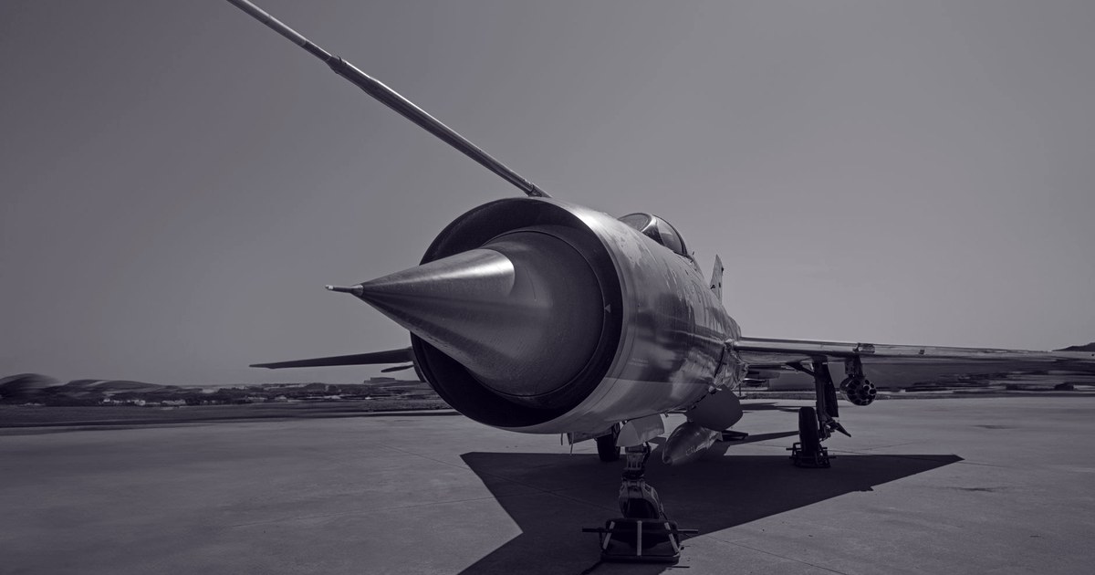 The nose cone and engine intake of a fighter jet, viewed head on from the tarmac, in black and white