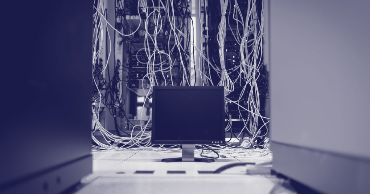 A dark data center corridor with a blank monitor screen surrounded by tangled network cables, no one present at the console