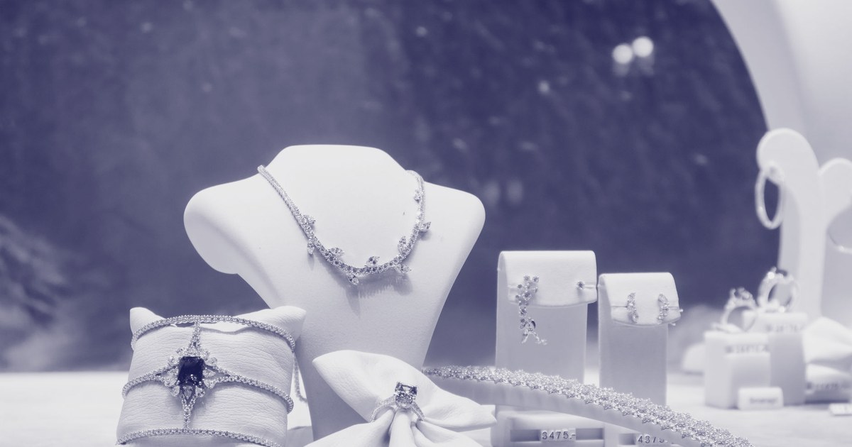 A jewellery shop window display with a necklace on a bust, a bracelet on a cushion and rings, lit in warm tones