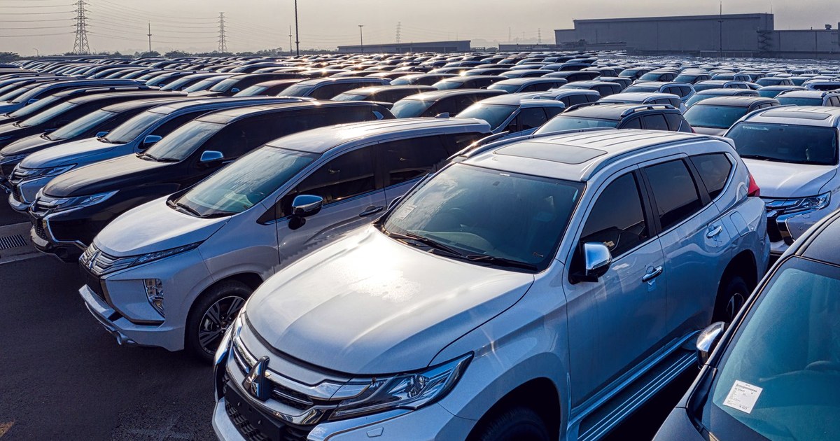 Rows of new SUVs parked in a vehicle storage lot beside a factory building at sunrise