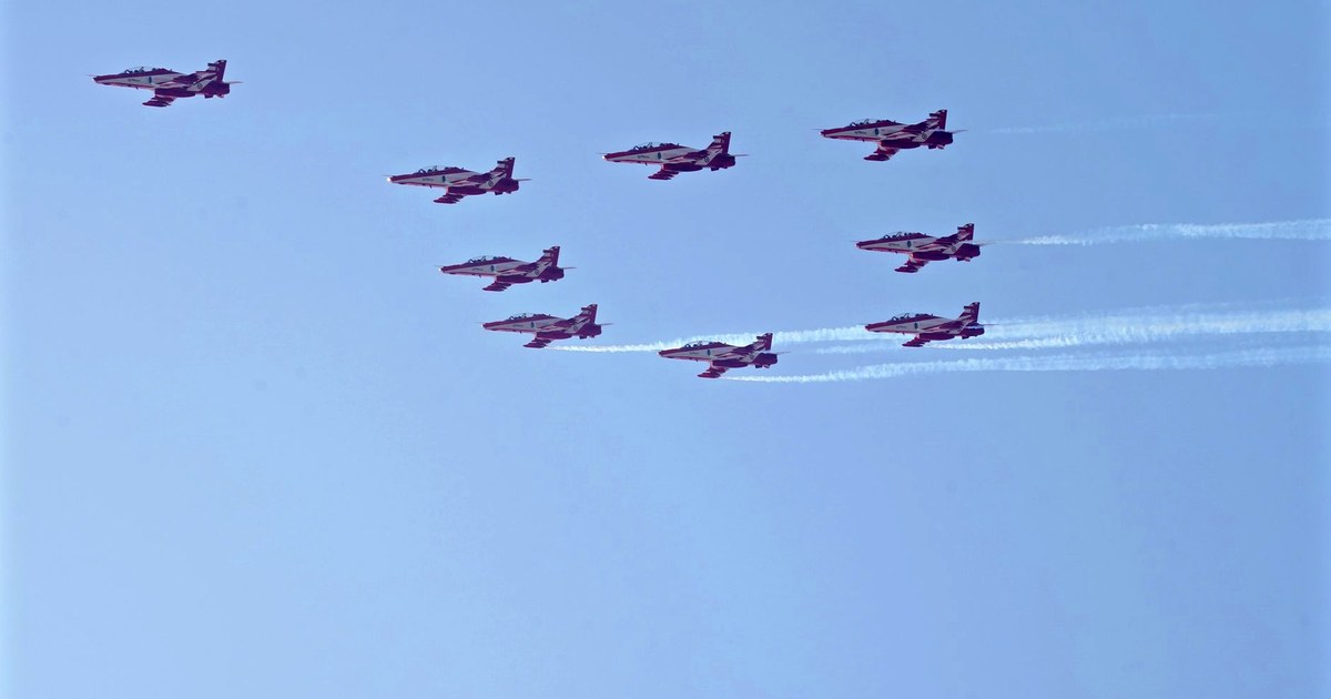 Nine red and white Suryakiran aerobatic jets of the Indian Air Force in formation against a clear blue sky, with white smoke trails