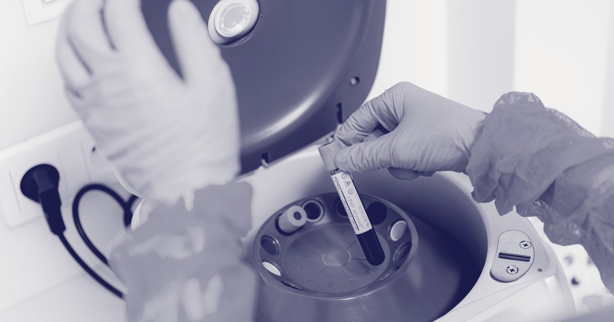 A gloved laboratory technician placing a sample vial into a centrifuge for analysis