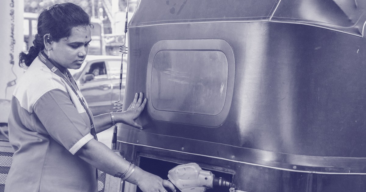 A fuel station attendant in a blue and yellow uniform refuels an auto rickshaw in India
