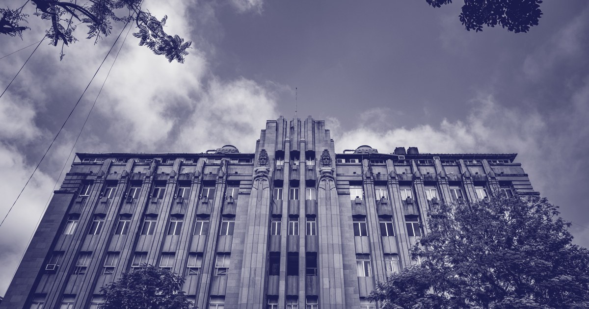 A tall Art Deco office building in Mumbai seen from below under a cloudy sky, shown in a blue duotone
