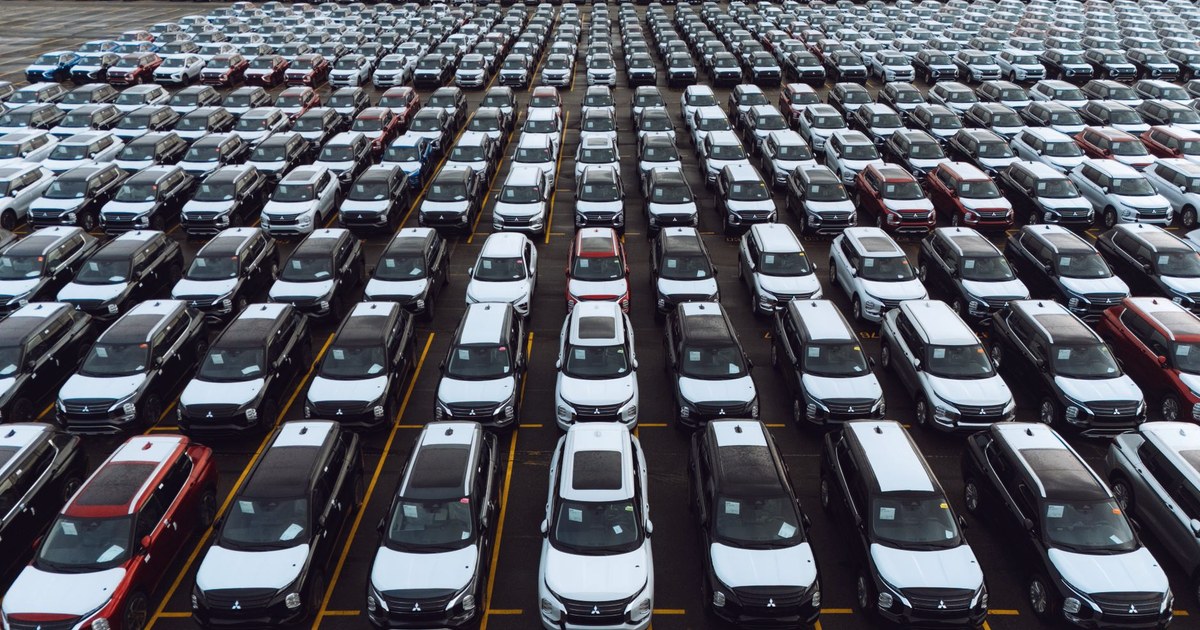 Aerial view of thousands of new cars parked in matching rows in a vehicle storage lot, awaiting delivery to dealers