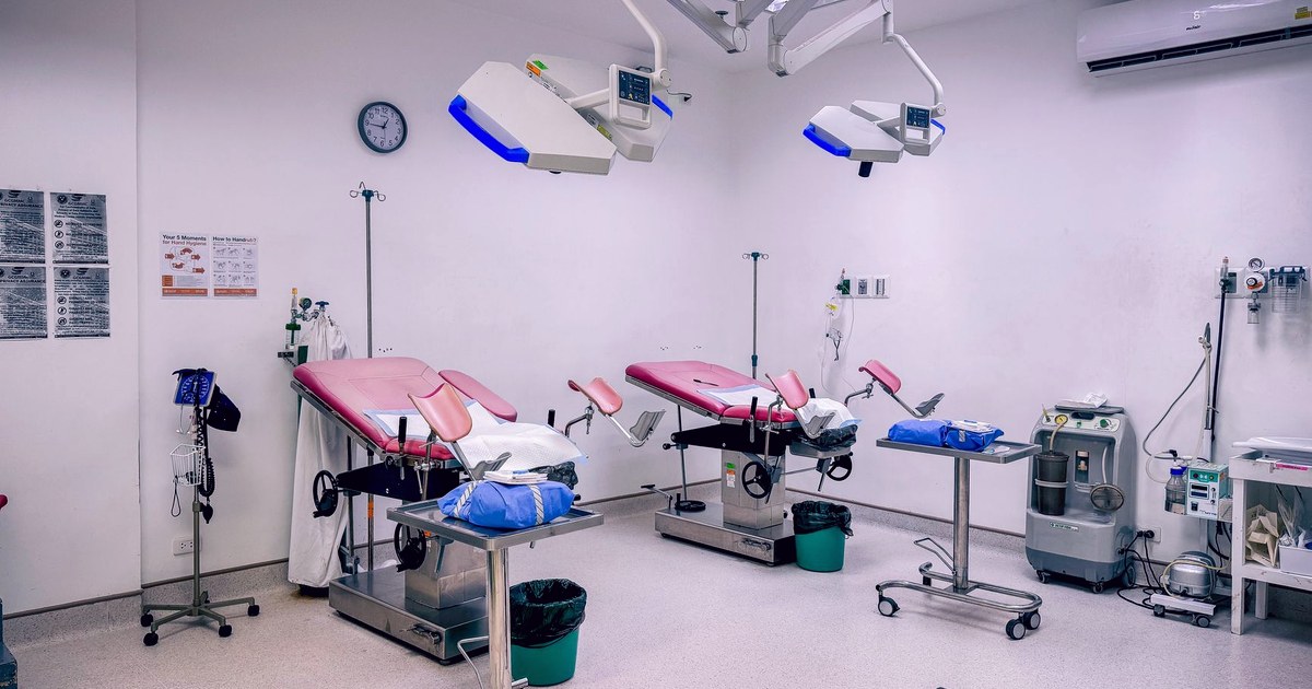 An empty hospital delivery room with two obstetric delivery tables under surgical lights, IV stands and monitoring equipment beside each