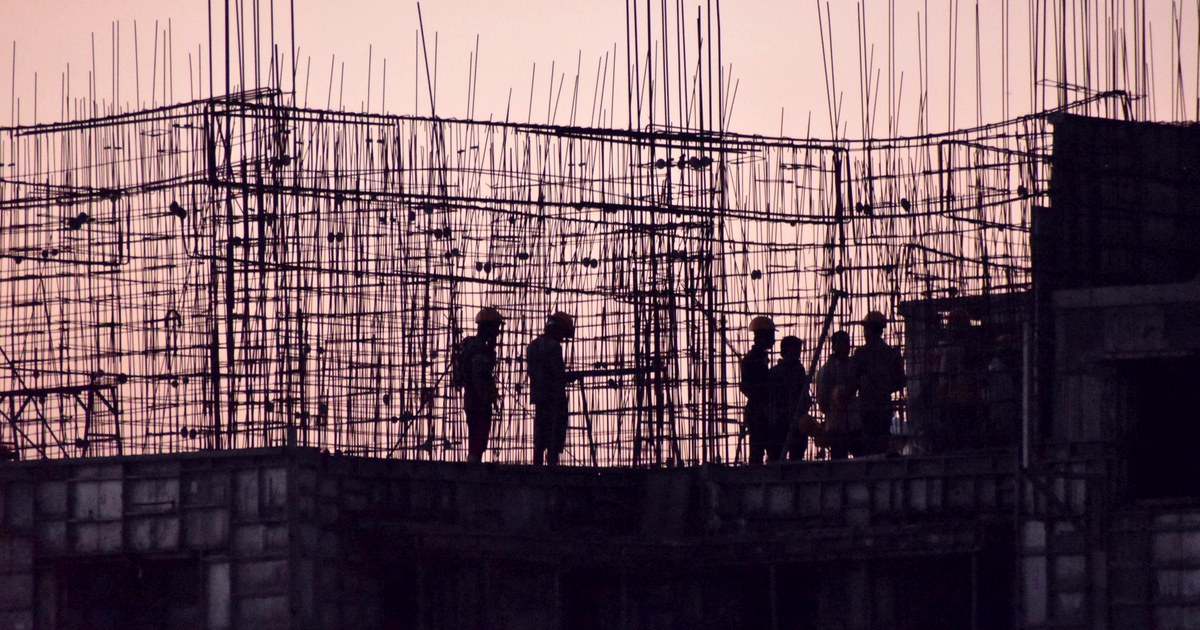 Silhouettes of construction workers on a concrete frame and steel rebar at sunset in India