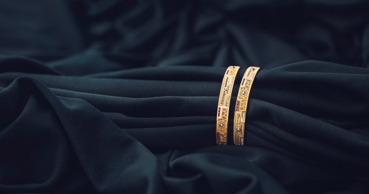 A pair of ornate gold bangles resting on dark green fabric