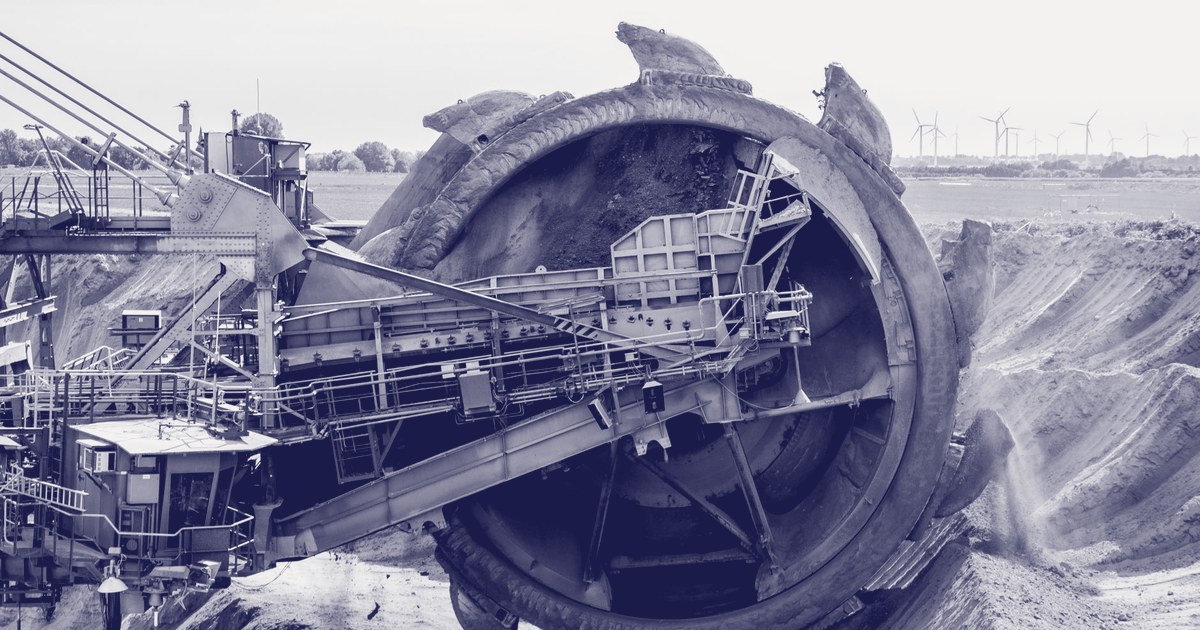 A bucket-wheel excavator working an open-pit mine, with wind turbines visible on the horizon