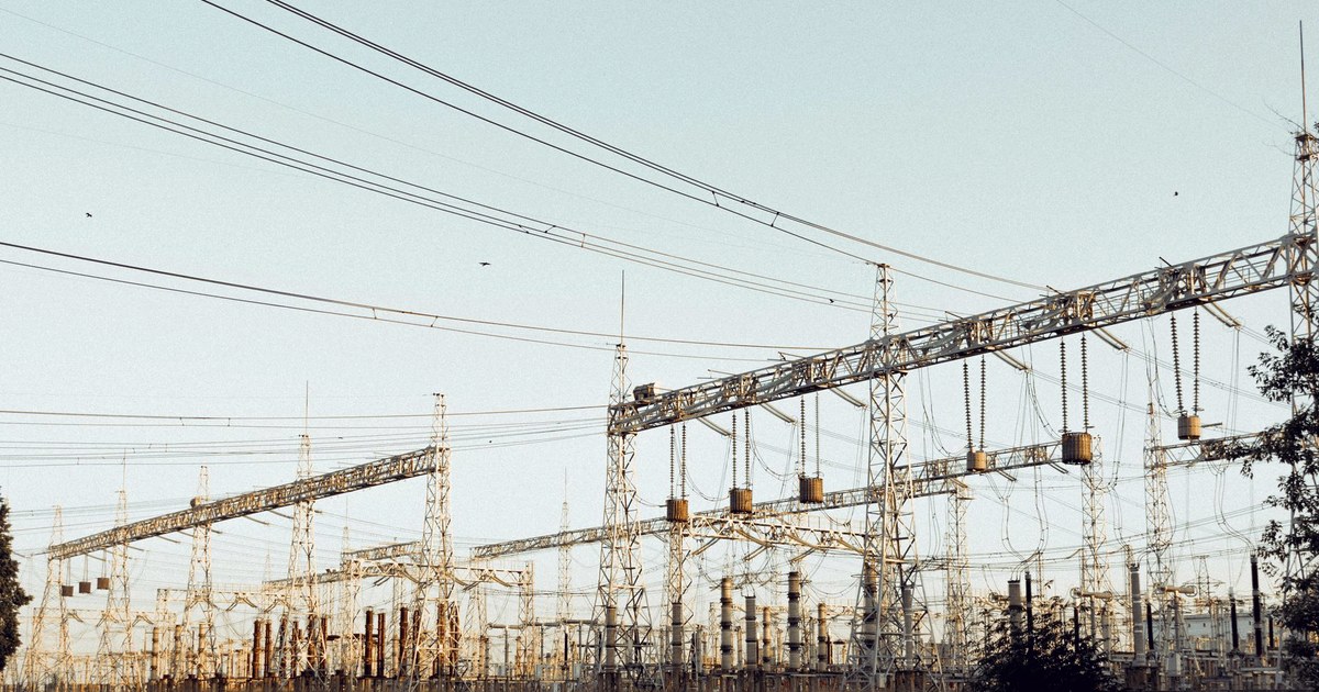 A wide view of an outdoor electrical substation with gantries, insulators and overhead power lines under a pale sky
