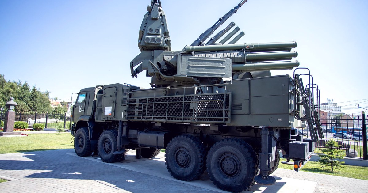 A green camouflage-painted, truck-mounted mobile air-defense system with radar and missile launch tubes, on outdoor display under a clear blue sky
