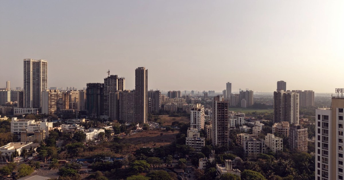 Aerial view of a dense Mumbai high-rise skyline in daytime haze, financial district towers rising above the wider city