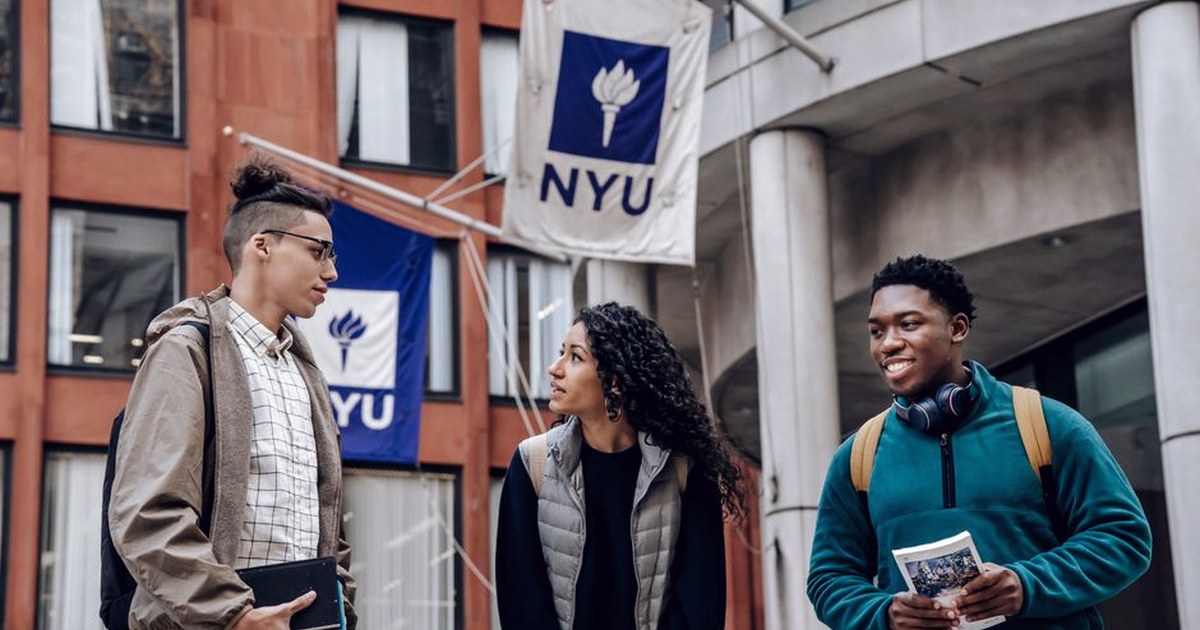 Three international students talking together outside a university building with NYU banners