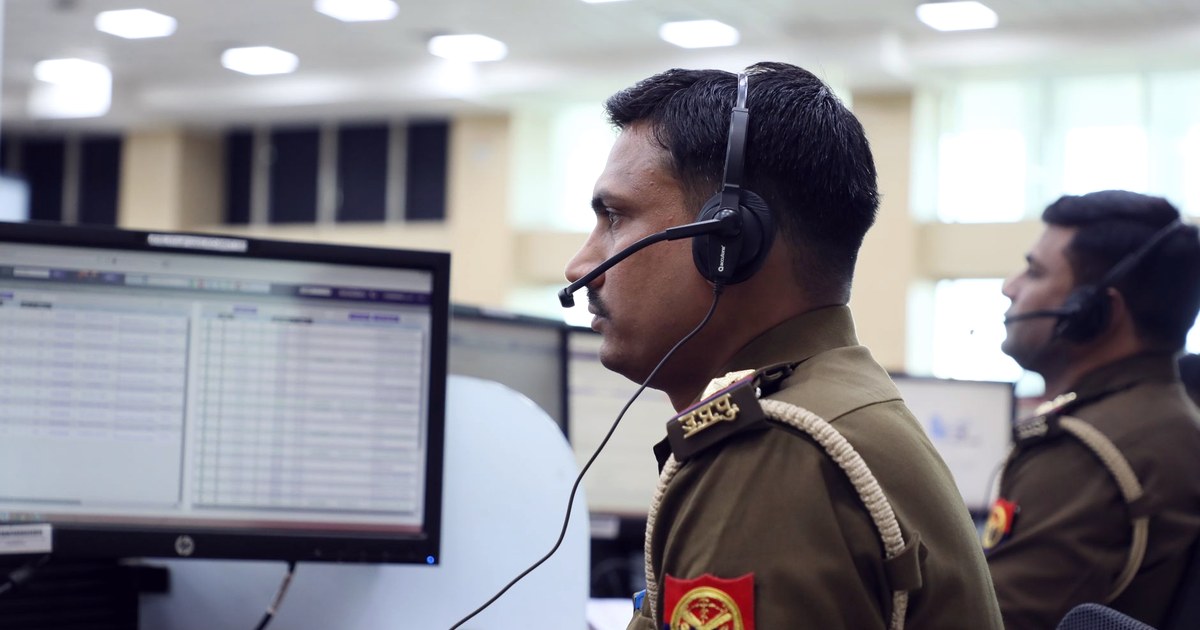 An Indian police officer wearing a headset works at a computer in a cyber crime monitoring center, with a colleague at a workstation behind him