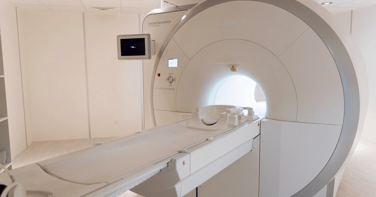 An empty MRI scanner in a hospital imaging room, the tunnel lit from inside and the patient table extended