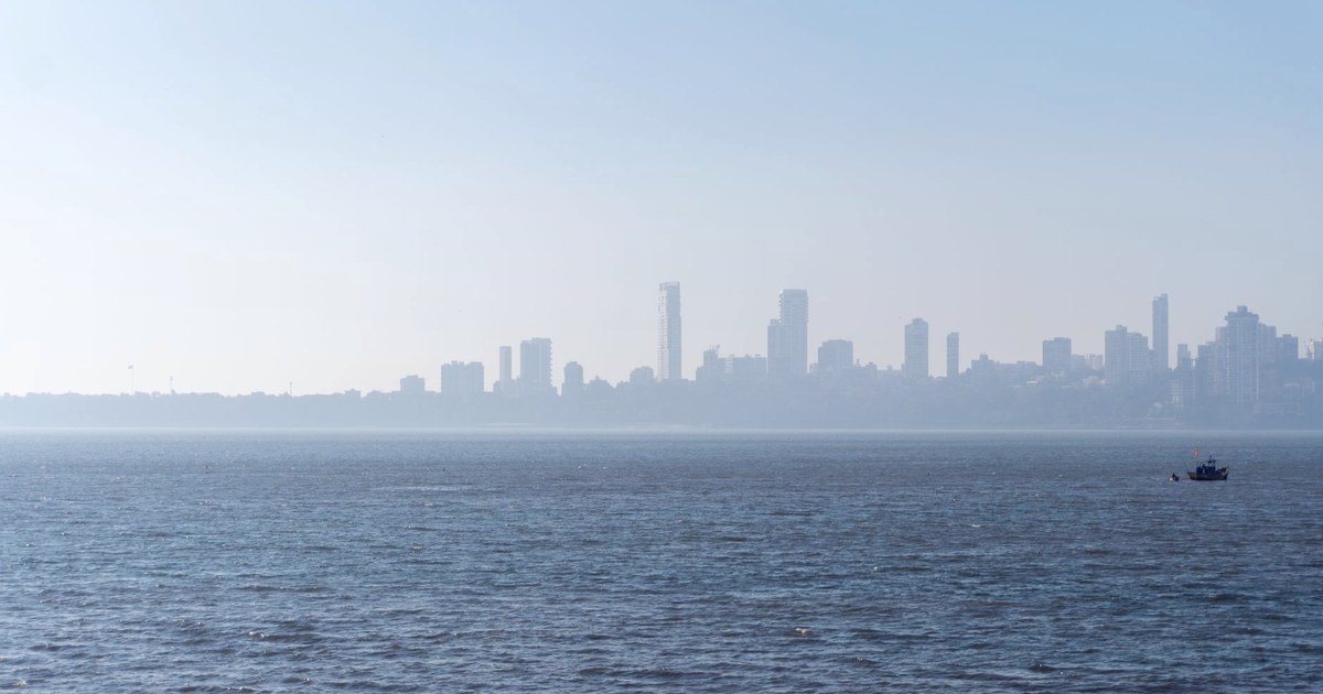 Mumbai's skyline seen hazily from across the sea, with a small fishing boat in the foreground