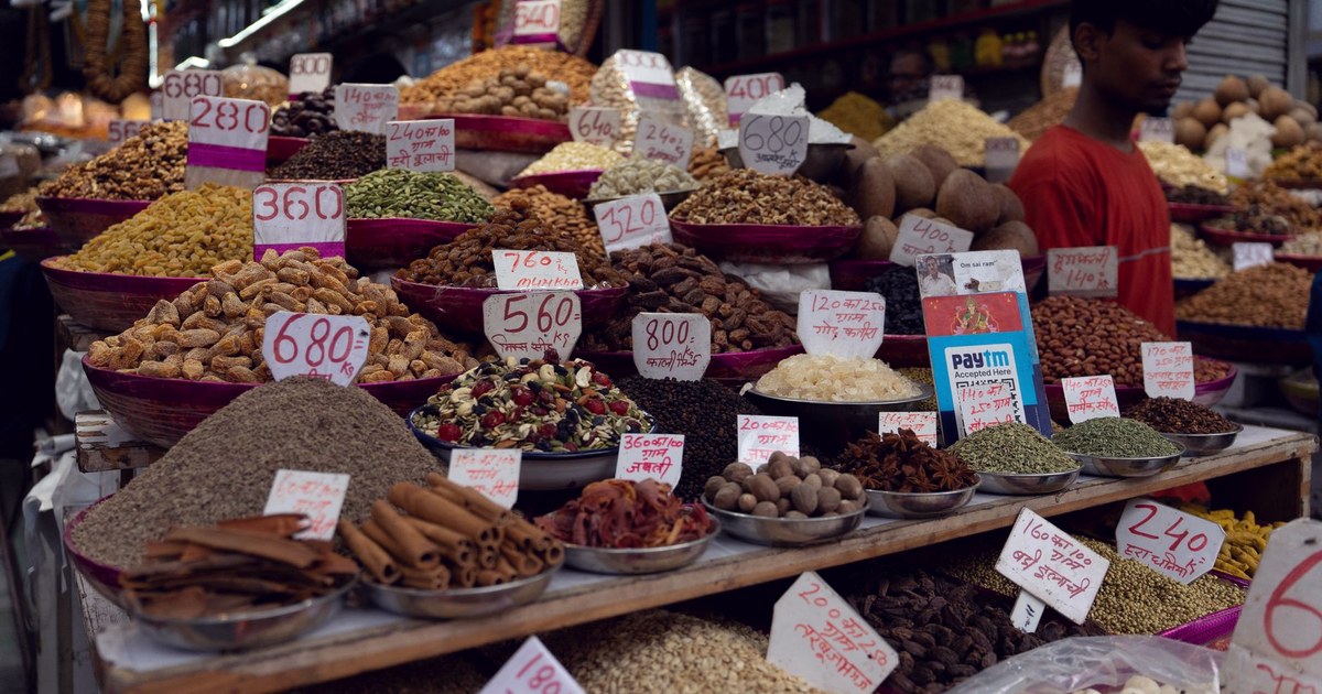 A vibrant spice and dry-goods market stall in India with hand-lettered price cards in rupees on baskets of nuts, seeds and dried fruit