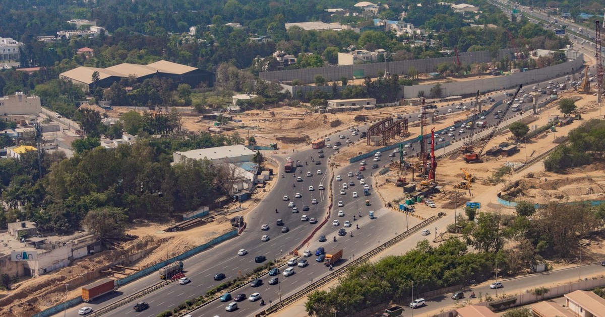 Aerial view of a Delhi expressway with active road and metro construction cranes alongside heavy traffic
