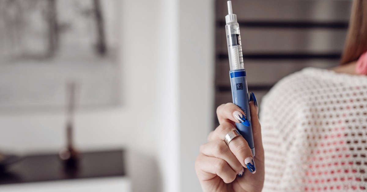 A woman holding a blue GLP-1 style injection pen in a bright, modern room