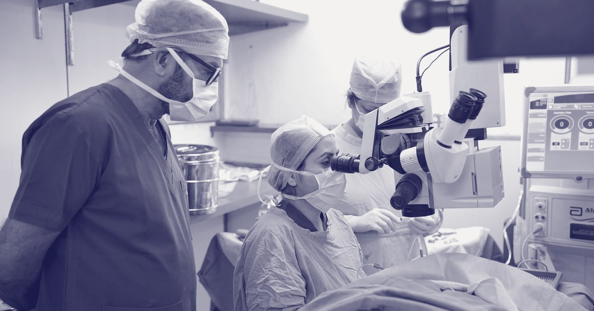Surgeons and an operating room team in blue scrubs working around an operating microscope during a procedure