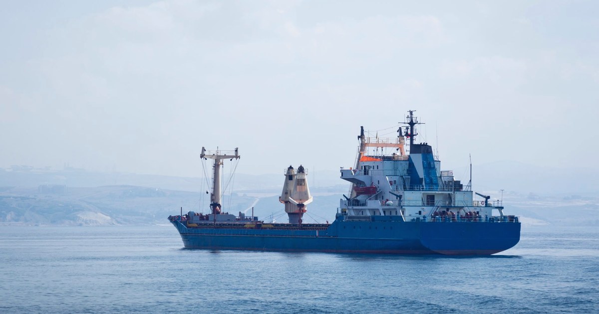 A blue cargo ship sailing on a calm sea near a hazy coastline