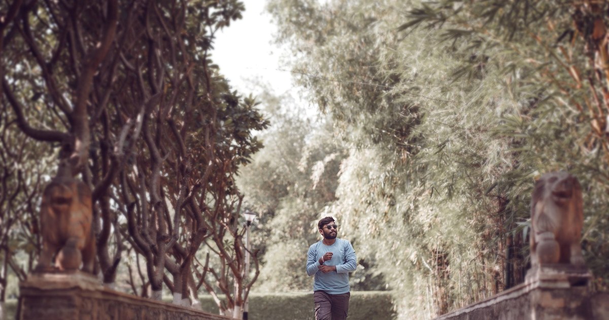 A man in a blue shirt and sunglasses walks along a tree-lined stone path in Surat, Gujarat