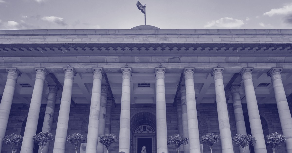 A columned sandstone government building in New Delhi with the Indian tricolour flying above its dome