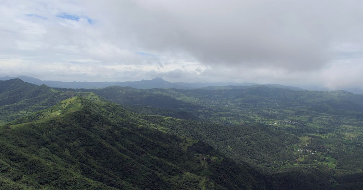 Aerial view of the lush green Sahyadri (Western Ghats) mountains near Pune, Maharashtra, with heavy monsoon clouds hanging over the ridgeline