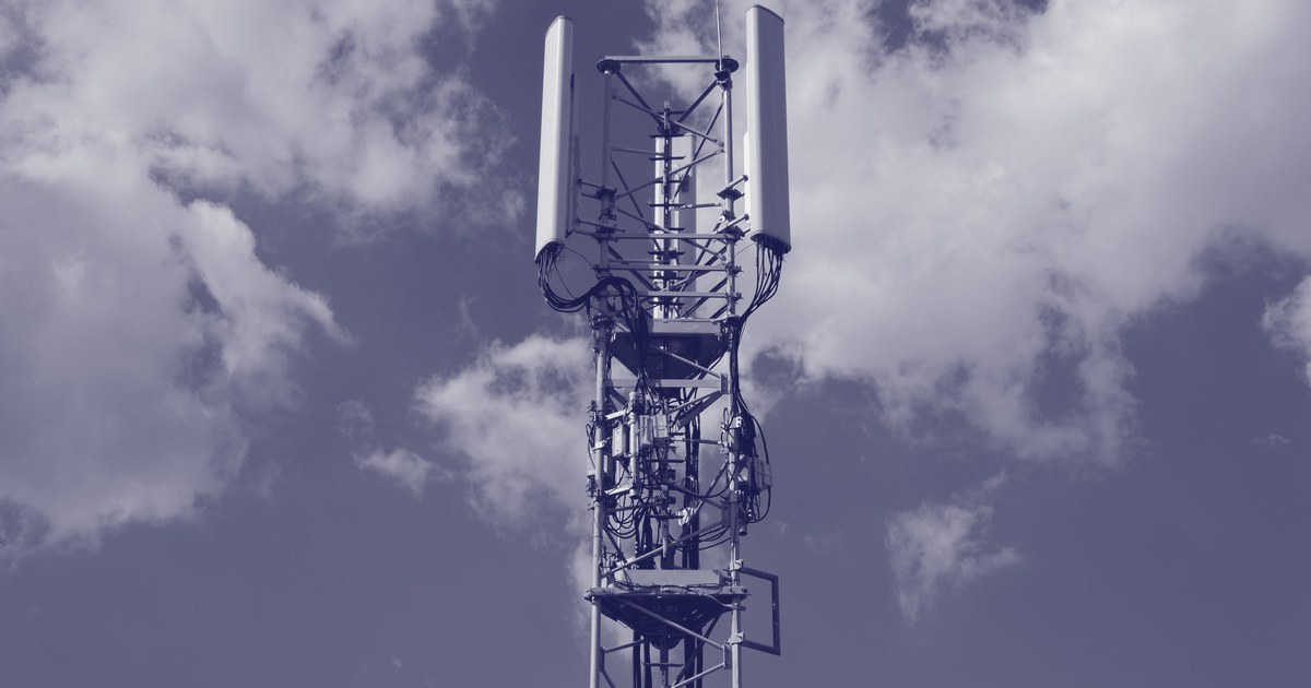 A cellular network tower with panel antennas rising against a blue sky with clouds
