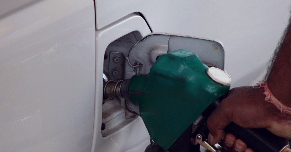 A hand holding a green fuel nozzle in the fuel inlet of a white car at a petrol station