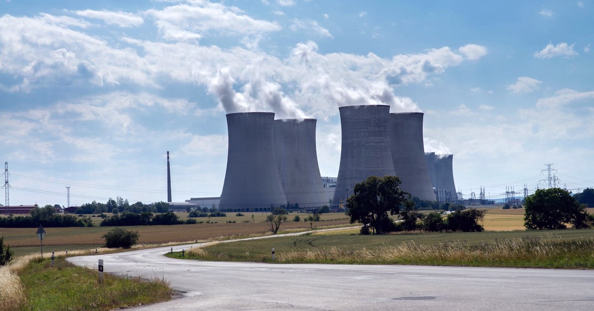 Cooling towers of a nuclear power plant releasing steam under a partly cloudy sky, seen from a rural road