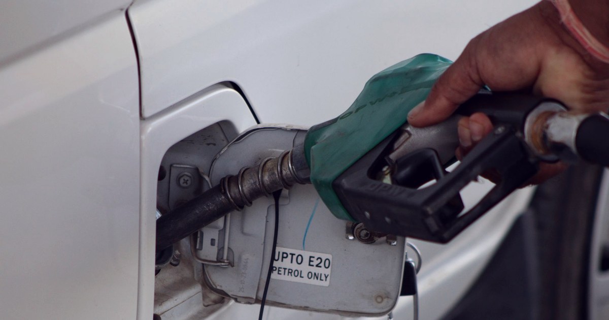 A hand refuels a car with petrol at an Indian fuel pump, with an 'Upto E20 Petrol Only' label visible on the fuel filler door