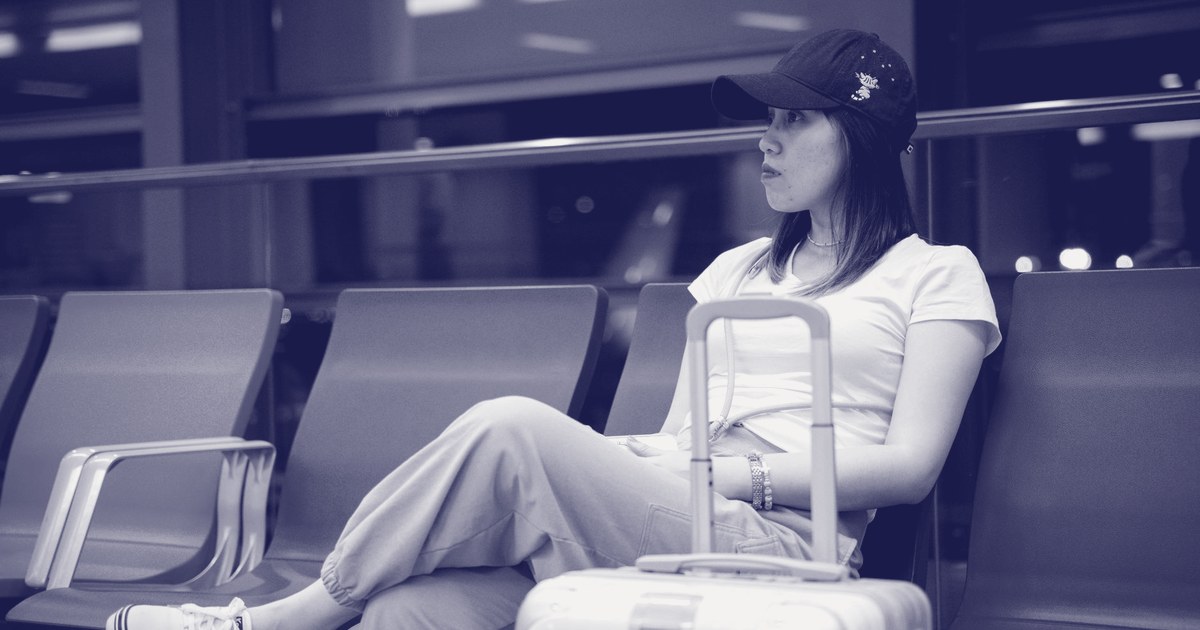 A traveler sits with luggage in an airport terminal seating area, waiting to depart.