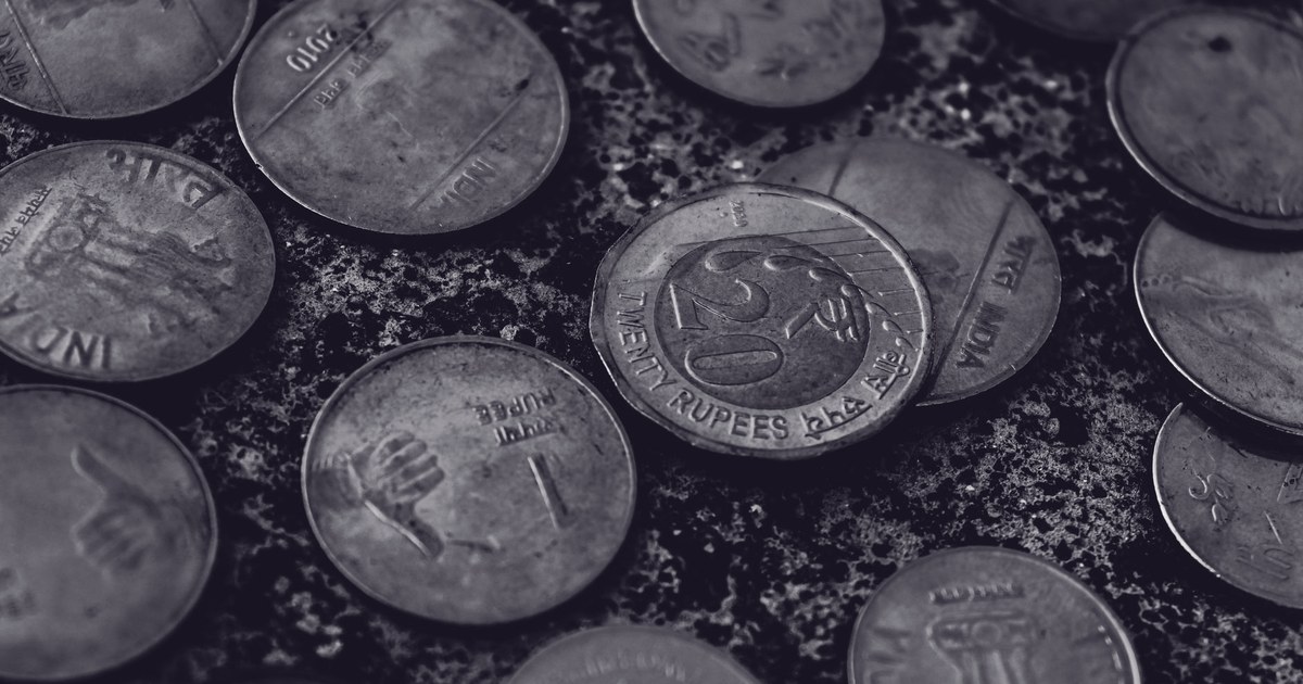 Close-up black and white photograph of scattered Indian rupee coins, including a twenty-rupee coin, on a rough stone surface