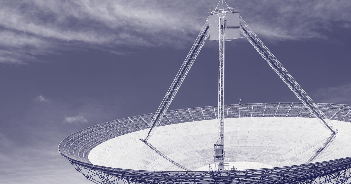 A large satellite dish photographed from below against a blue sky with wisps of cloud
