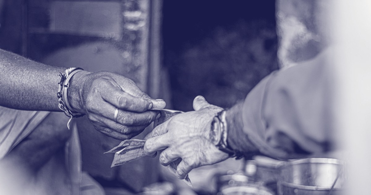 Two hands exchanging Indian rupee cash notes at a small roadside tea stall