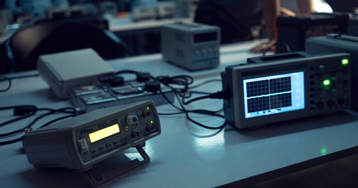 A signal generator and an oscilloscope displaying a synchronized waveform on a lab bench, with engineers working in the background