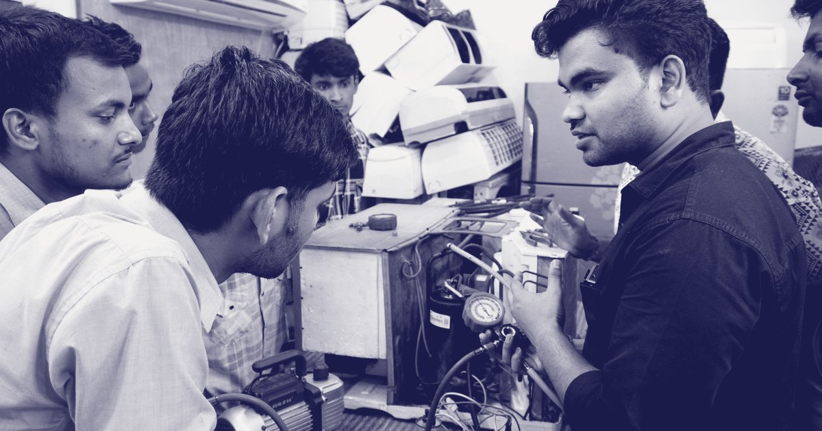 Trainees and an instructor examining an air-conditioning unit during a hands-on vocational repair session in Delhi