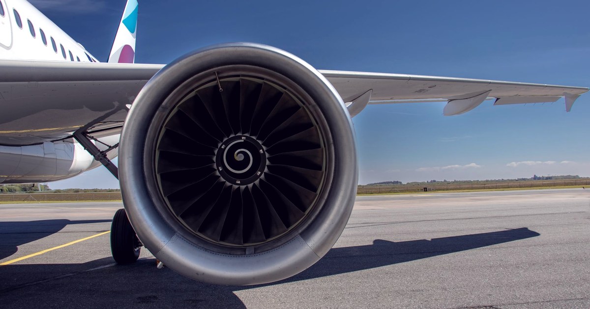 Close-up of a commercial jet engine and wing against a clear blue sky, with the aircraft's tail visible in the background