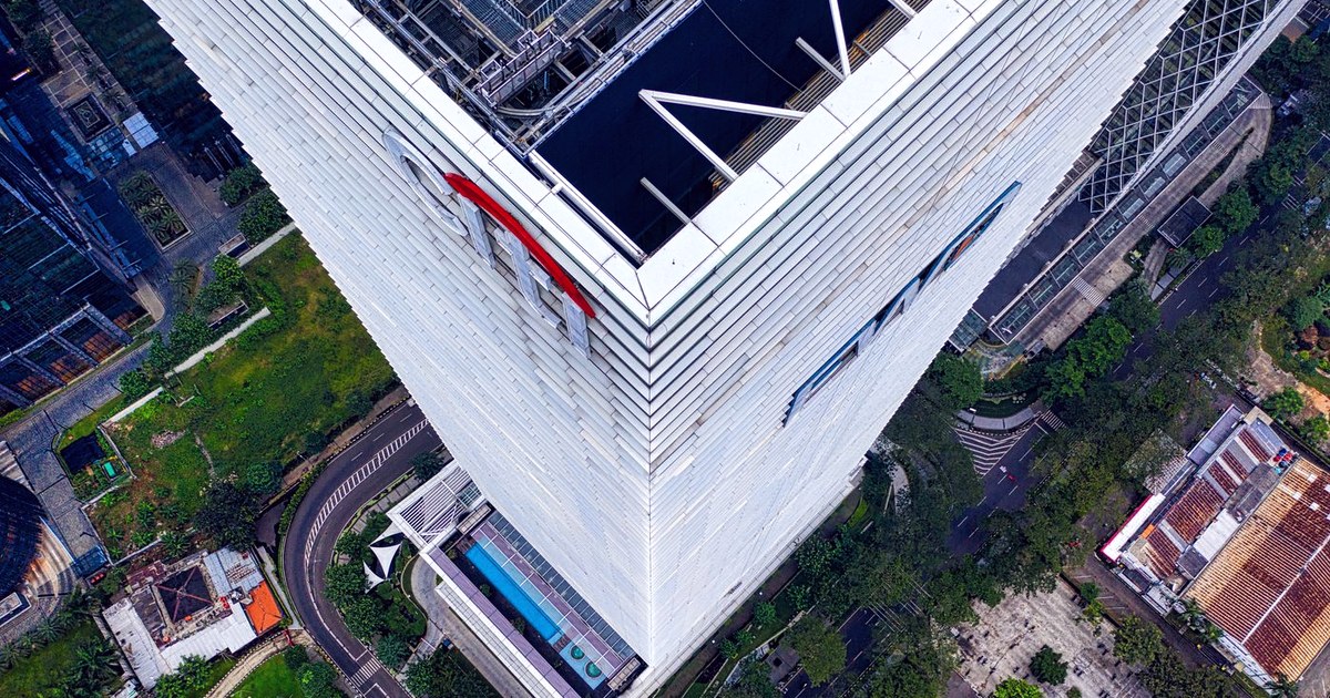 Aerial view looking straight down at the corner of a white skyscraper in Jakarta, with roads, trees and a parking lot below